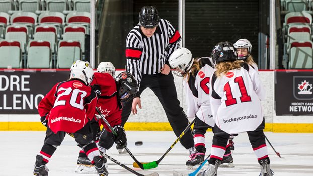 An official drops a puck during a faceoff during a game between young students.