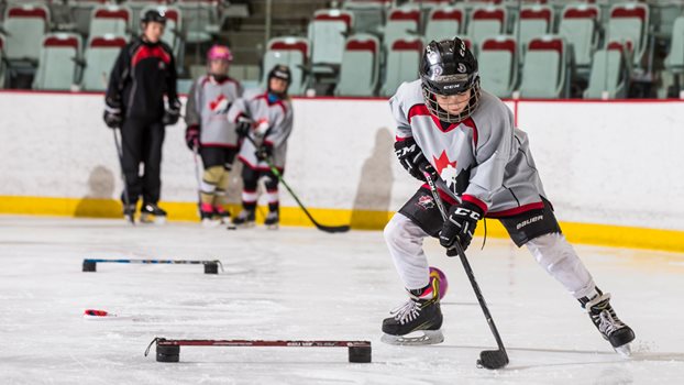 A young hockey player focuses on controlling the puck during a drill.