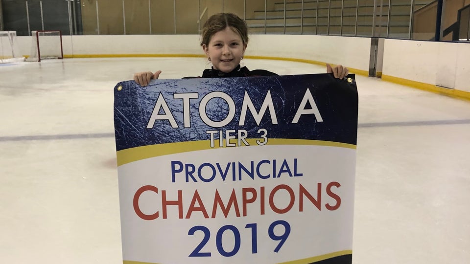 Marissa holds a banner that says Atom A Provincial Champions 2019