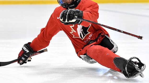 Para hockey player skating in a sled wearing a red Hockey Canada practice jersey.