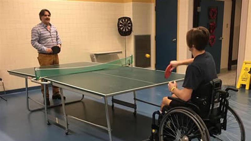 Vincent Boily, assis dans son fauteuil roulant, joue au tennis de table avec son père, Érick Boily.