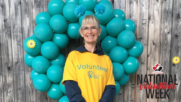 Susan Sloan wearing a shirt that says Volunteer in front of a balloon arch.